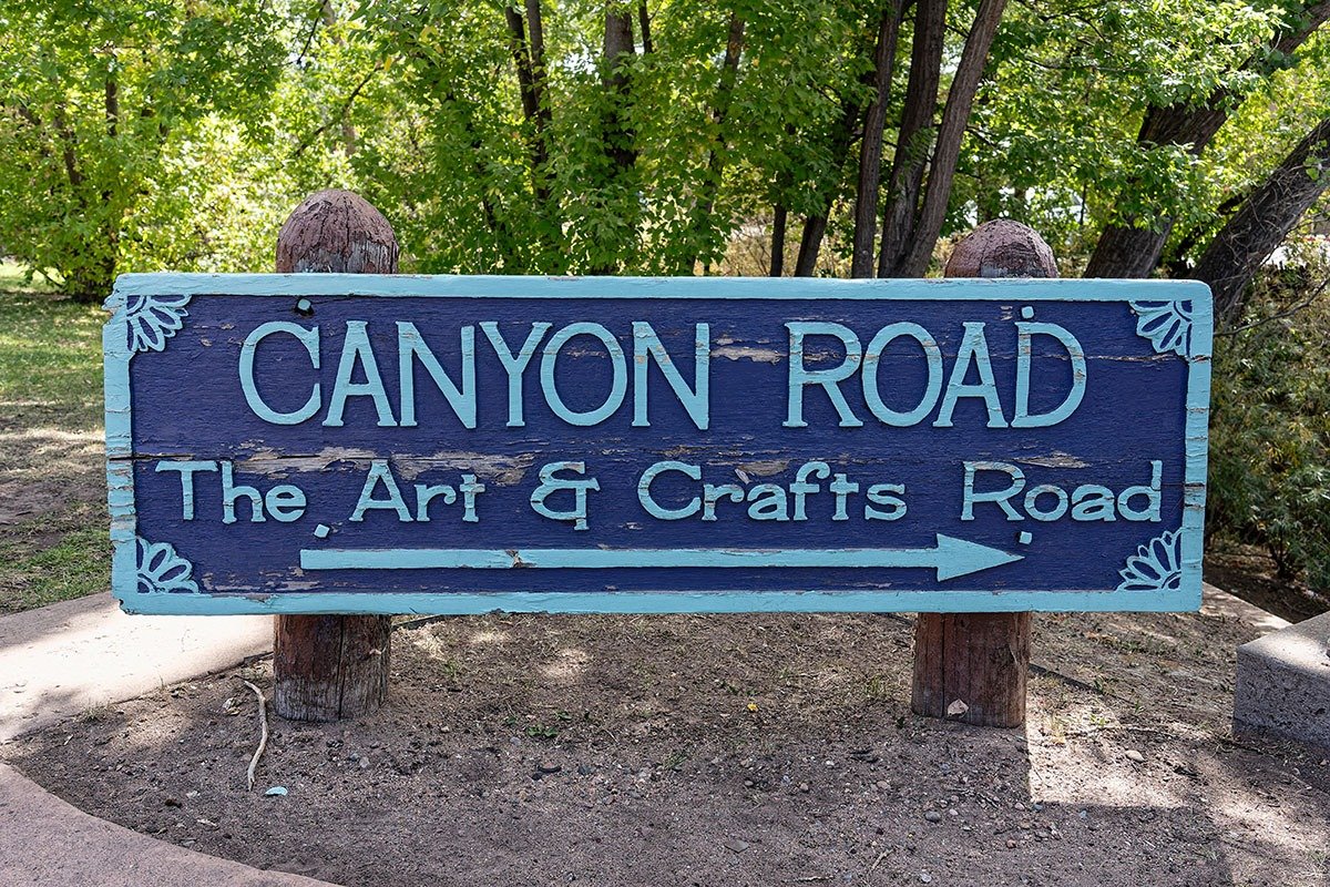 A wooden sign reads 'canyon road' with an arrow pointing to the right, surrounded by greenery.