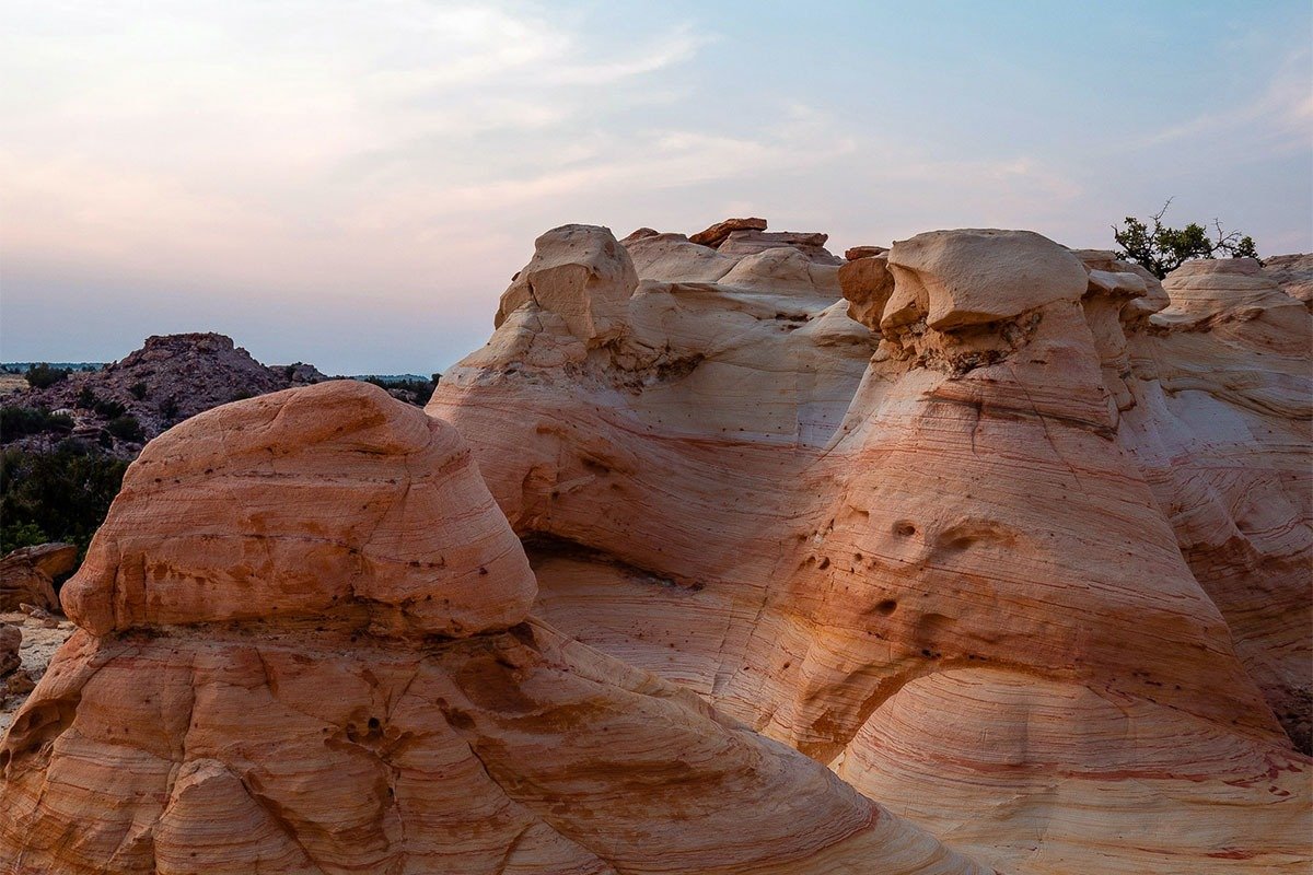 Rock formations with layered orange and white stripes under a pastel sky at dusk.