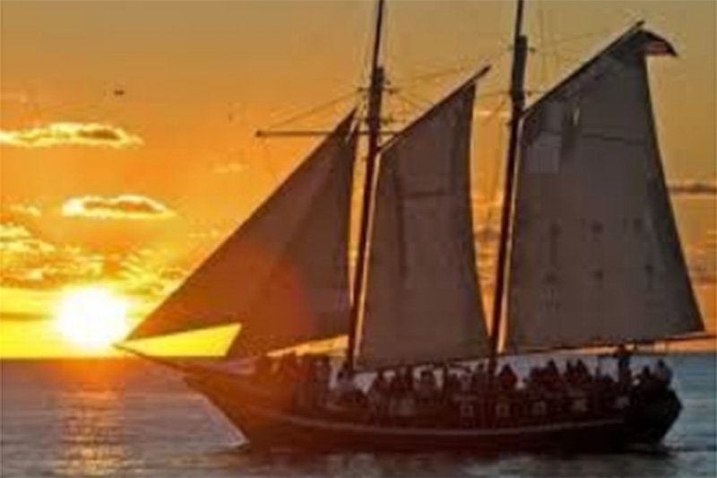Sun setting behind sail boat on ocean