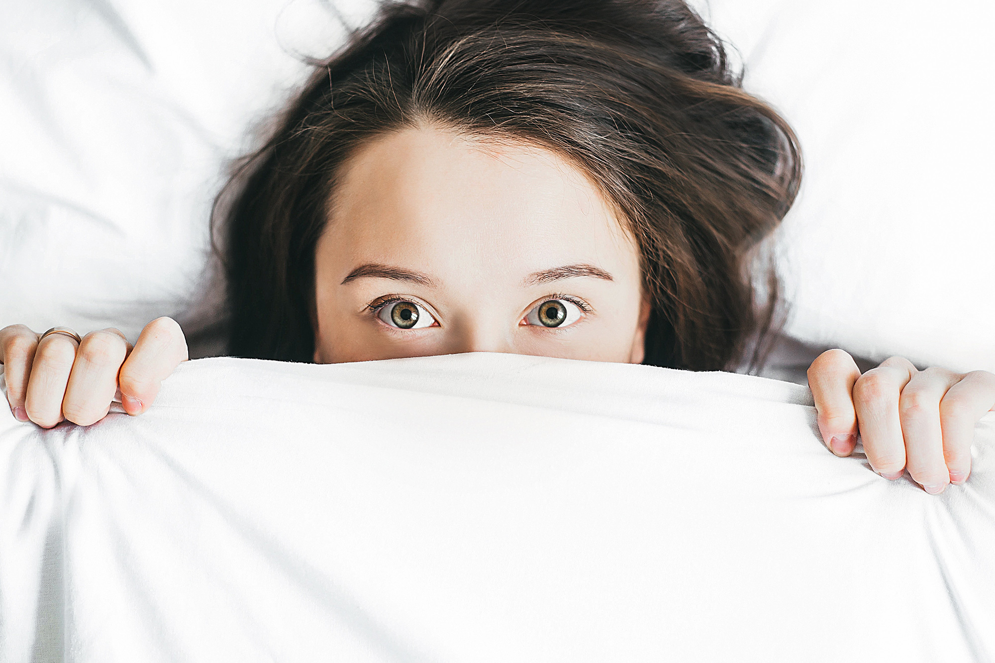 woman peeking out of white comforter